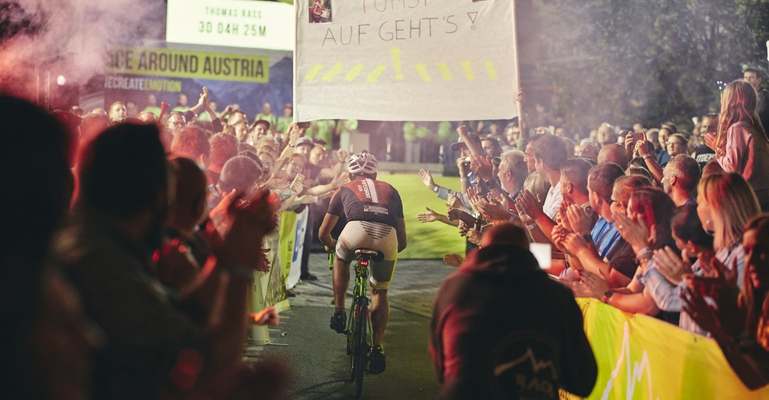 Zieleinlauf eines Radfahrers beim Race Around Austria mit tausenden Fans bei Nacht. 
